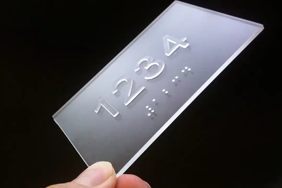 a woman's hand holding up an example of a translucent plastic sign with braille